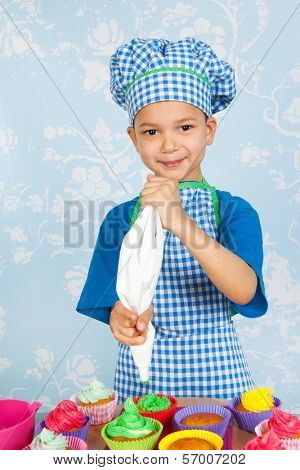 Little boy is baking colorful cupcakes with vintage wall paper in background