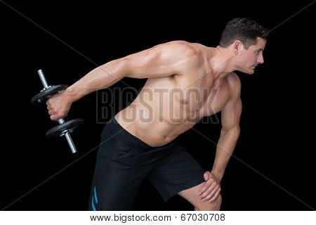 Strong crossfitter lifting heavy black dumbbell behind him on black background