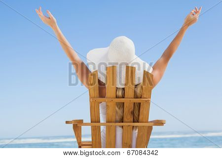 Woman sitting in deck chair at the beach with arms up on a sunny day