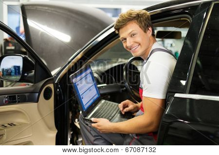 Serviceman making car diagnostics with laptop in a workshop