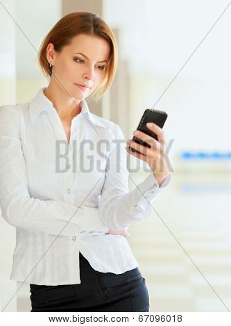Young busineswoman standing with phone in office lobby