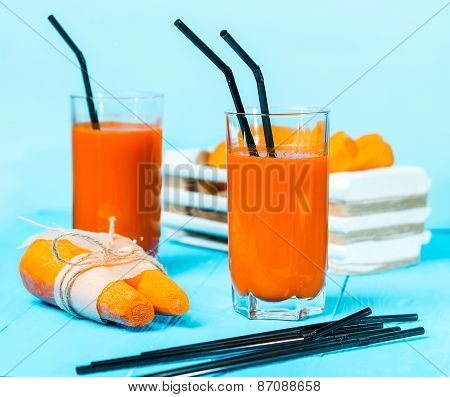 Freshly squeezed carrot juice in the glasses.A box with purified carrot on a blue wooden background.