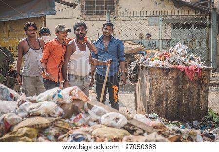 MUMBAI, INDIA - 16 JANUARY 2015: Five adult garbage men pile up garbage on slum street before throwing into garbage truck. Post-processed with grain, texture and colour effect.