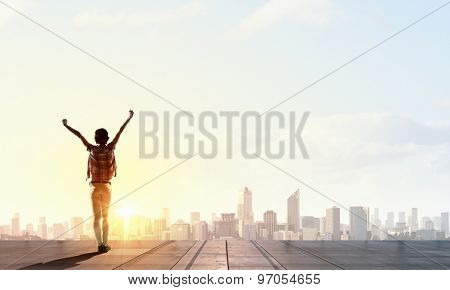 Rear view of girl with hands up facing sunrise abone city