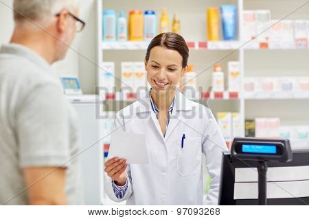 medicine, pharmaceutics, health care and people concept - pharmacist reading prescription and senior man at drugstore cash register