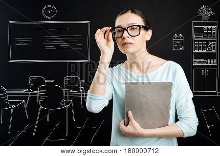 Switch on curiosity. Pleasant professional teahcer looking forward and holding textbook while working at school