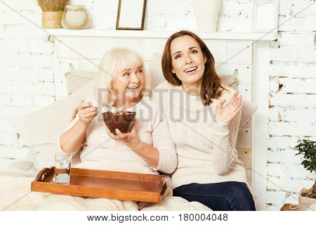 Discussing life with my grandmother. Thoughtful charming young woman sitting at home and taking care of retired grandmother while pensioner enjoying breakfast