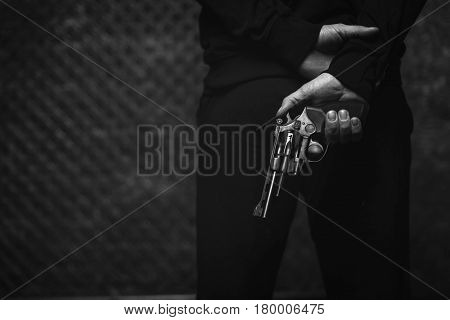 Plotting a crime. Lawless scary hateful villain holding a gun in his hand hiding it behind his back while waiting for his victim