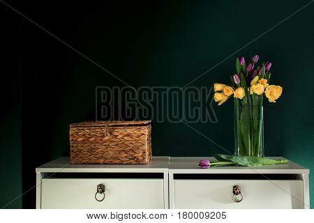 yellow daffodil flowers with pupple tulip blooming in vase with green wall. Dark key. Interior with candle