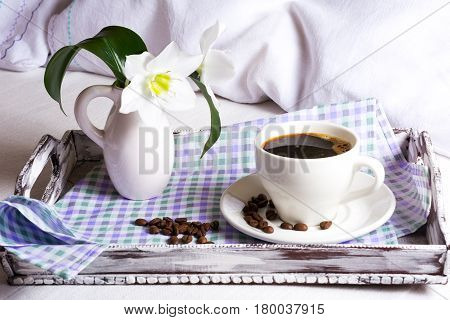 Morning coffee in bed with white lily flowers in vase on rustic wooden serving tray. Tender love concept.