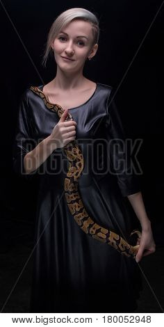 Blond woman in leather dress with python on black background