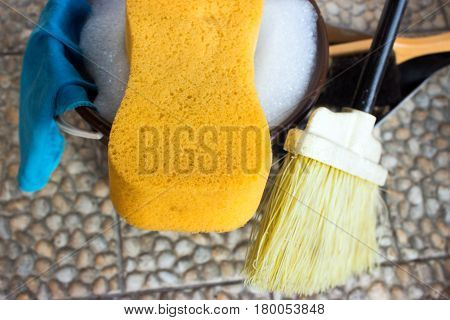 Bucket with water and soap. Sponge is in foreground and rights is broom and dustpan. Left on the bucket is hung rag.