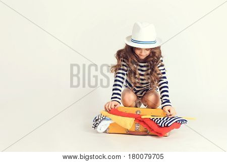 Young girl is trying persistently to close up overloaded with her clothes suitcase. The picture is taken at studio and has white background