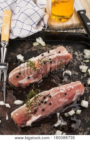 raw pork belly stripes with thyme onion olive oil and meat fork on a roasting tray