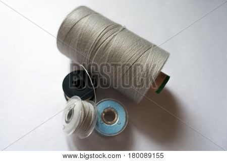 Spools of thread (grey, blue, white) on neutral background