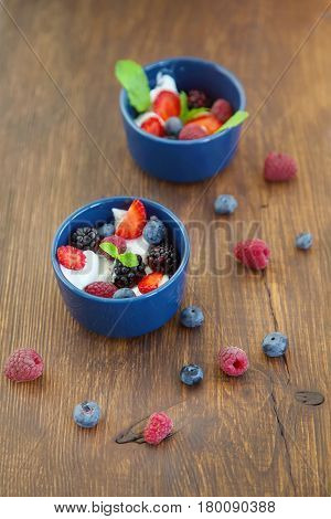 Milk fruit dessert. Whipped cream with berries. Serving tasty treats from dairy cream different berries and mint on the wooden table. Blue cup with cream berries and mint.