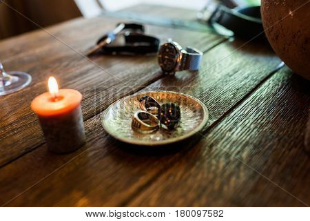 Bronze plate with men's rings on a wooden table with burning candles. Men's accessorizes, necktie, watch