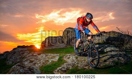 Cyclist Riding the Mountain Bike Down Spring Rocky Hill at Beautiful Sunset. Extreme Sports and Adventure Concept.