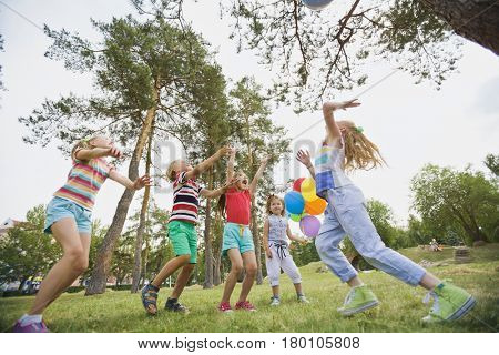 Low angle view of excited children playing games with beach ball in city park on a summer day