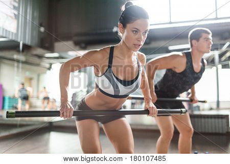 Portrait of strong muscular woman doing squat exercise with body bar in gym, man in background
