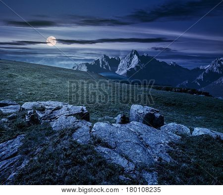 Composite night landscape with full moon. rocky peaks of mountain ridge and rocks on hillside under the dark sky with clouds and stars. picturesque fantasy view.