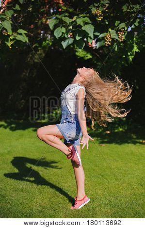 Girl with Long Blowing Hair is jumping at a green park in summer. Glamour Beautiful girl with Healthy and Beauty Blond Hair. Beautiful hair concept.