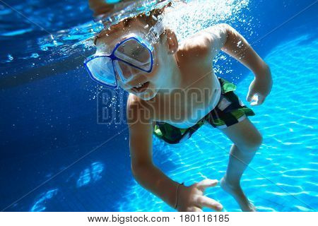 Happy boy swims underwater in swimming pool with snorkel mask