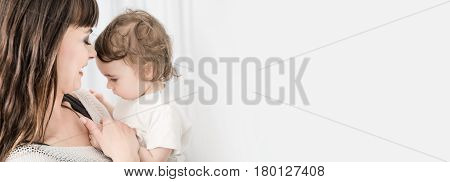 Young beautiful and smiling mother with baby girl. Daughter close to loving mom. Copy space for your text.