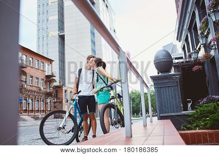 Young people, couple with bicycles on the street. A loving couple on a date on a summer evening. The guy with the girl hugs and kisses. Youth, first feelings, first love, first dates
