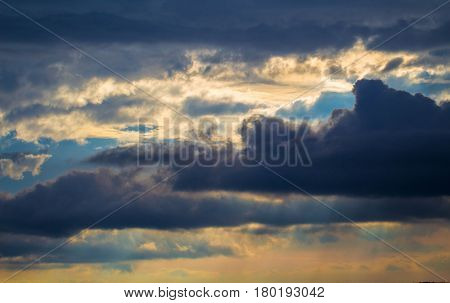 Stormy sky with rays of sunlight. Sunset scene with rainy clouds. Tropical sunset romantic photo banner. Fluffy clouds with sun reflections. Orange sunlight on grey clouds. Rainy season weather