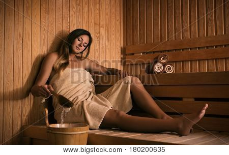The young beautiful girl relaxes in a sauna and plays with water.