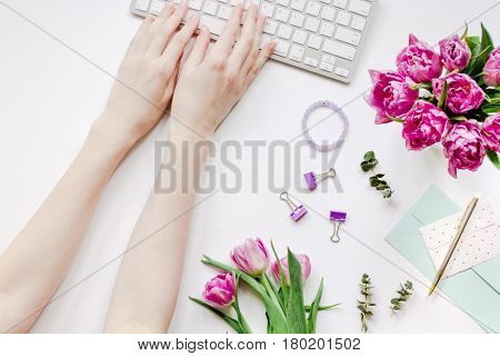 Spring pink flowers and hands on workdesk at home ofiice white background top view