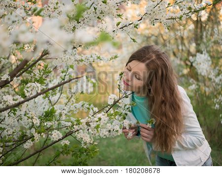 outdoor portrait of a beautiful woman in white jacket among white blossom tree.