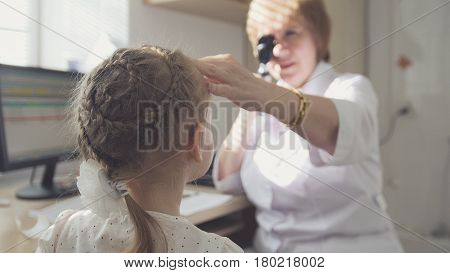 Woman optometrist in clinic checks eyesight at little girl - child's ophthalmology, telephoto