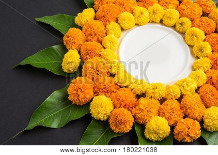 flower rangoli made using marigold or zendu flowers and mango leaves over black background with copy space in the middle, selective focus