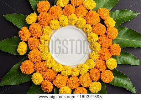 flower rangoli made using marigold or zendu flowers and mango leaves over black background with copy space in the middle, selective focus