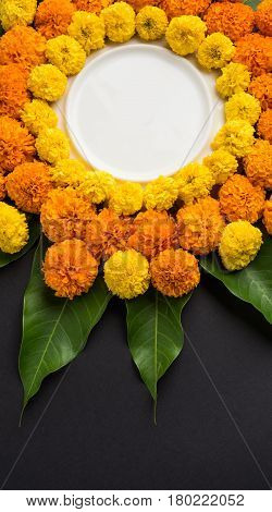 flower rangoli made using marigold or zendu flowers and mango leaves over black background with copy space in the middle, selective focus