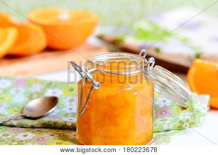 Delicious orange jam. Homemade orange jam in a glass jar, spoon, textile napkin, orange slices on a table. Healthy citrus dessert. Closeup