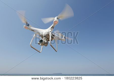KAGAWA, JAPAN - APRIL 03, 2017: White remote controlled Drone Dji Phantom4 Pro equipped with high resolution video camera hovering in air with shore and blue sky in the background