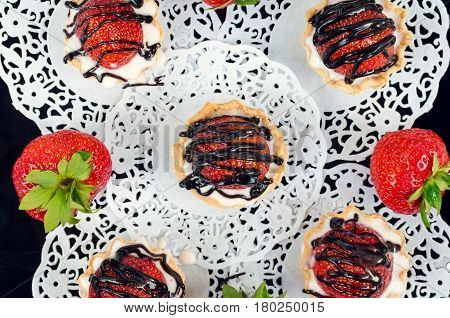 Strawberry cake with vanilla cream on white rusric wooden background. Sweet basket tartlet with strawberries and chocolate. Tasty summer dessert. Top view.