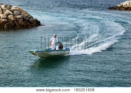 Man in traditional arabic thawb ride a speedboat near a coast in Oman 18.april 2012