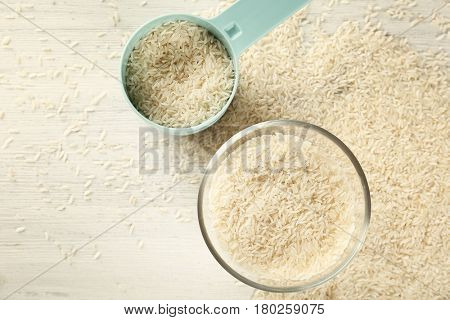 Lot of rice in bowl and measuring scoop on wooden table