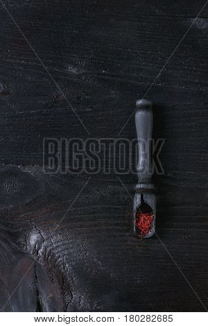 Raw Organic Red Saffron spice in wooden spoons over black burnt wood background. Top view with space