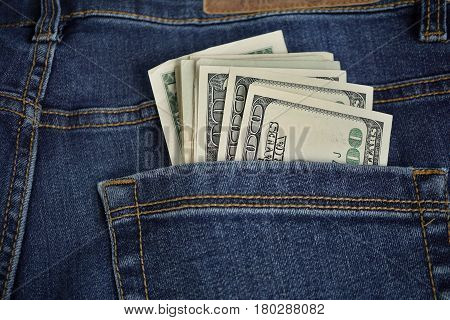 Heap of American money (US currency, USD) in the back pocket of blue jeans with yellow stitching as a symbol of black money earned without taxation