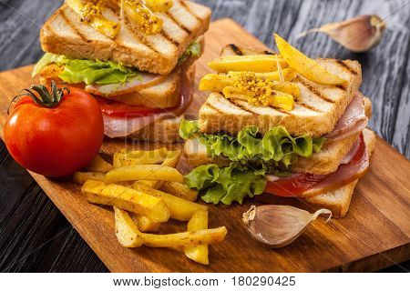 club sandwich with Tomato lettuce bacon ham and french fries on the black wooden table