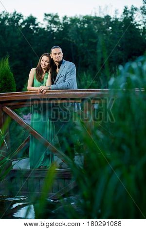 Bride and groom near lake. Evening nature walk of amazing couple. Couple posing in stylish clothes. Nice evening walk of amazing couple in the park.