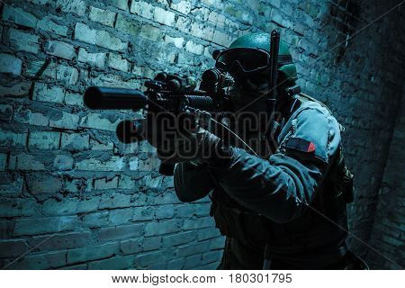 Special forces operator pointing weapon in the dark. Combat helmet, tactical radio system with folding antenna are on. Low key image