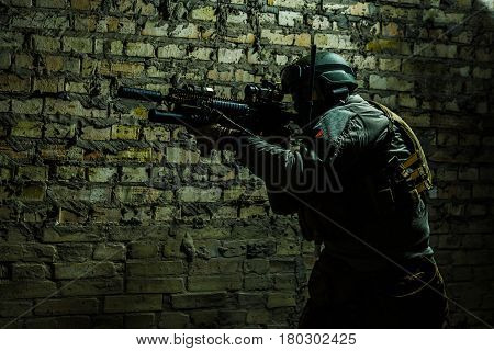 Special forces operator pointing weapon in the dark. Combat helmet, tactical radio system with folding antenna are on. Low key image
