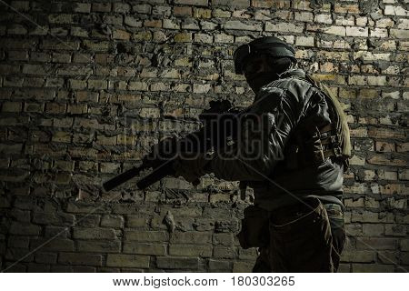 Special forces operator pointing weapon in the dark. Combat helmet, and bulletproof vest are on. Low key image, shadow soldier