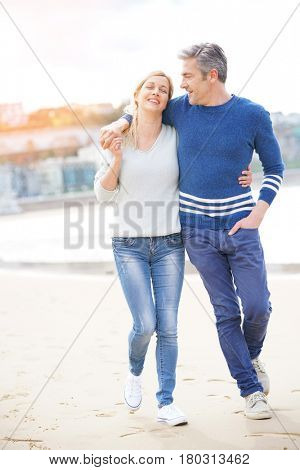 Middle-aged couple walking on the beach, full length